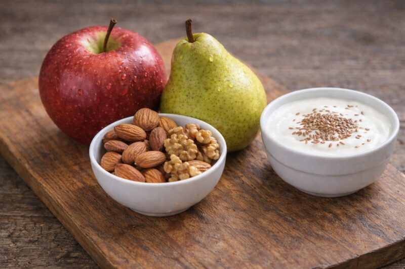 Jabuka i kruška sa bademima, orasima i jogurtom posutim lanenim semenom na drvenoj podlozi